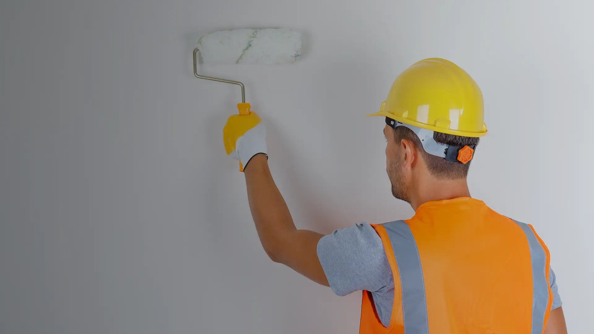 Equipe uniformizada pintando parede em obra comercial, com equipamento de proteção